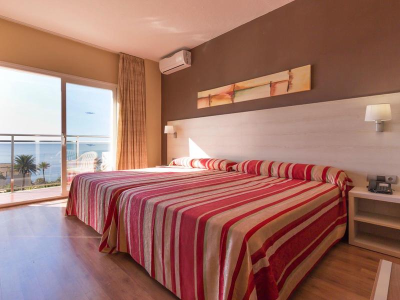 Hell eingerichtetes Hotelzimmer mit zwei Betten, Balkontür und Blick aufs Meer.