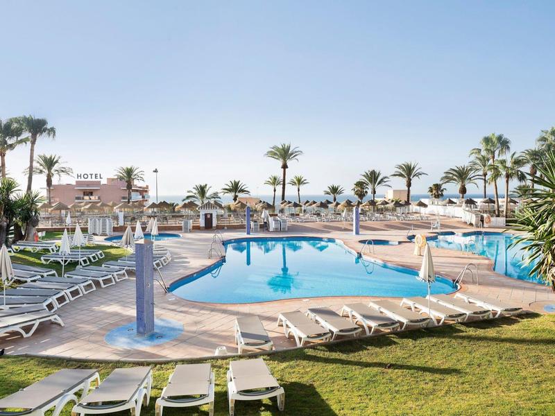 Freier Pool mit weißen Liegestühlen, Palmen und blauem Himmel im sonnigen Resort.