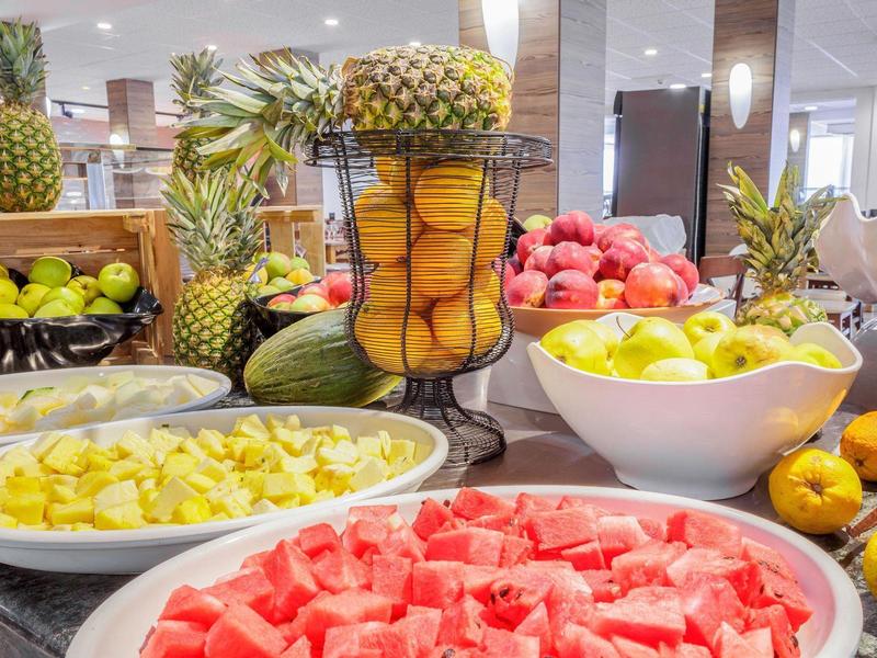 Bunter Obsttisch mit Wassermelone, Ananas, Orangen, Äpfeln und Mango in Schalen und Körben.