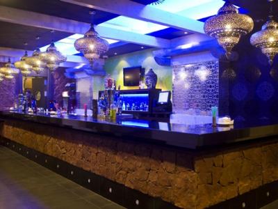 Moderner Barbereich mit dunklem Holz, Steinverkleidung und goldenen Hängelampen in blauem Licht.