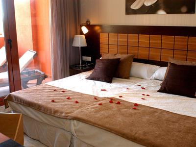 Gemütliches Schlafzimmer mit großem Bett, dekorativen Kissen und Balkon mit Liegestuhl.