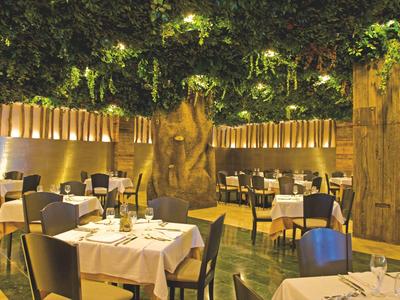 Restaurant mit weißen Tischtüchern, schwarzen Stühlen und grünem Hängepflanzen-Dekor an der Decke.