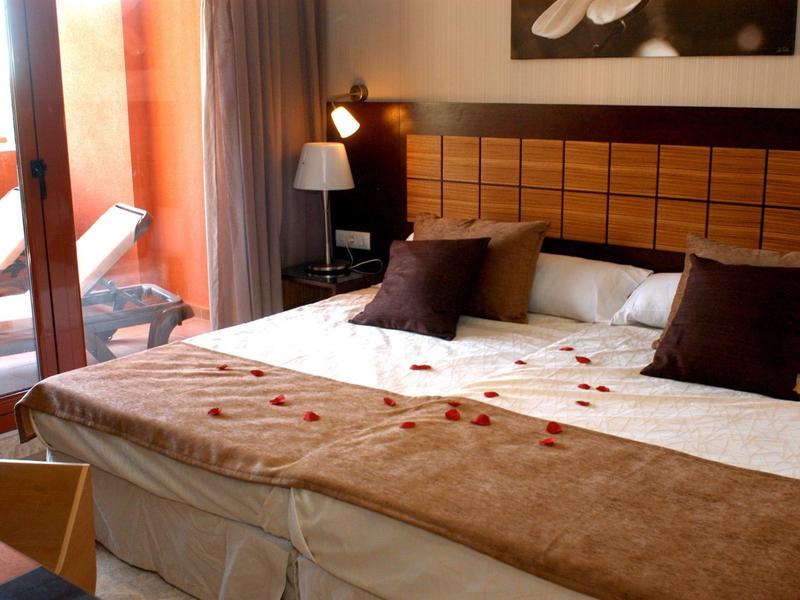 Gemütliches Schlafzimmer mit großem Bett, dekorativen Kissen und Balkon mit Liegestuhl.