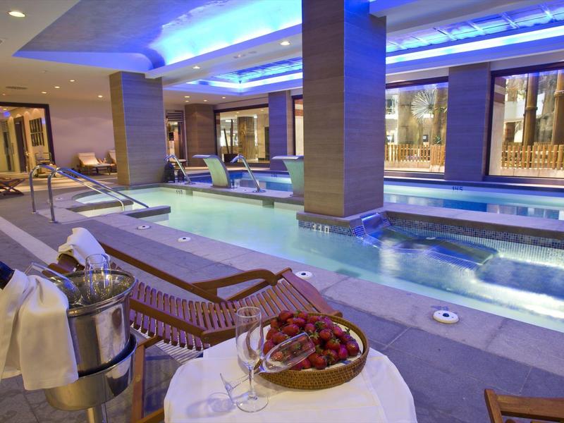 Luxus-Hallenbad mit warmem Licht, Liegestühlen, Champagner und Erdbeeren auf rundem Tisch.