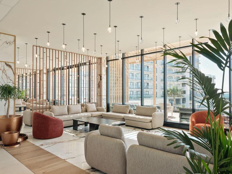 Modernes, lichtdurchflutetes Wohnzimmer mit großen Fenstern, Pflanzen und minimalistischen Möbeln.