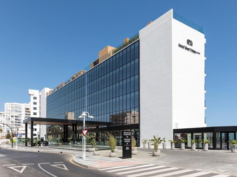 Modernes, rechteckiges Gebäude mit Glasfassade und weißer Außenwand unter blauem Himmel.