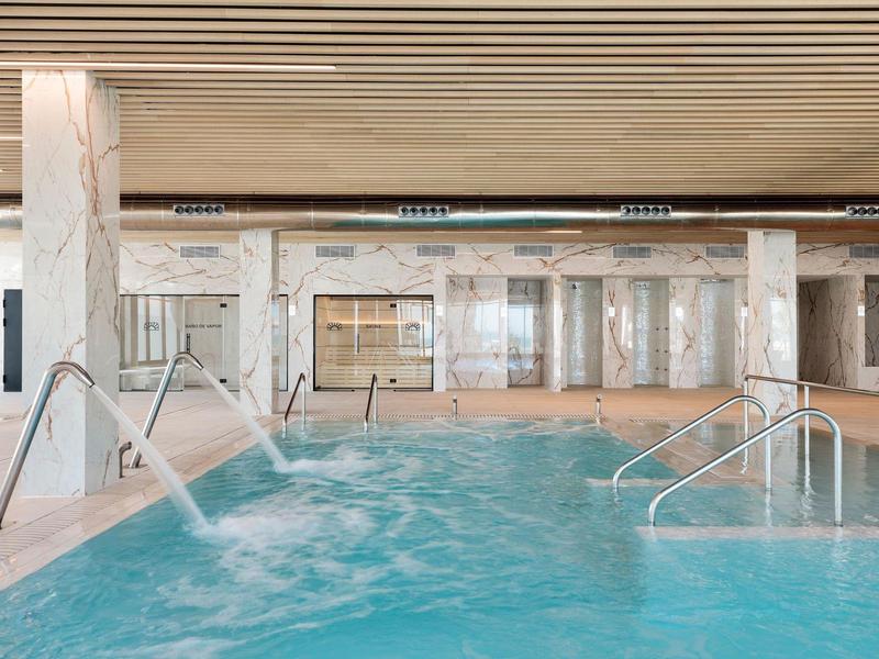 Innenpool mit klarem Wasser, Wasserspielen und hellem Holzdeckendekor in modernem Spa-Bereich.
