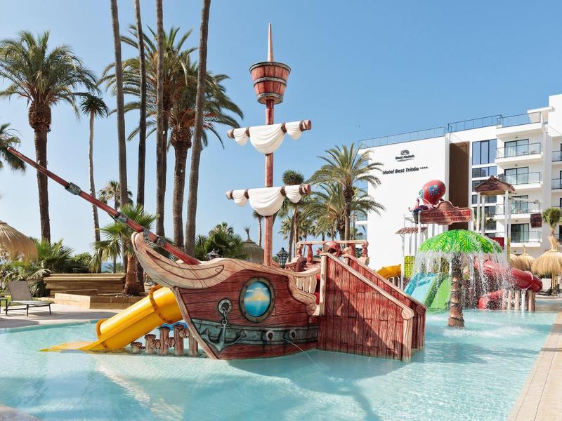 Buntes Piratenschiff mit Rutsche im Wasserpark, umgeben von Palmen und Gebäuden bei klarem Himmel.