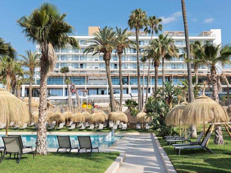 Moderner Hotelkomplex mit Palmen, Sonnenschirmen und Liegestühlen im Gartenbereich.