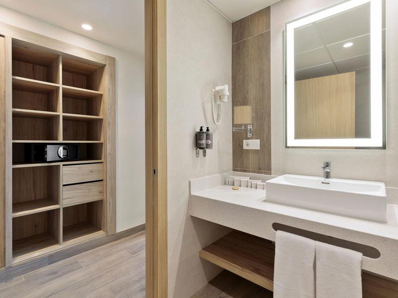 Helles Badezimmer mit großem Spiegel, integriertem Waschbecken und offenem Holzeinbauschrank.