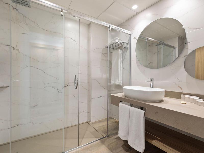 Modernes Badezimmer mit Glasdusche, runder Spiegel, großem Waschbecken und hellen Fliesen.