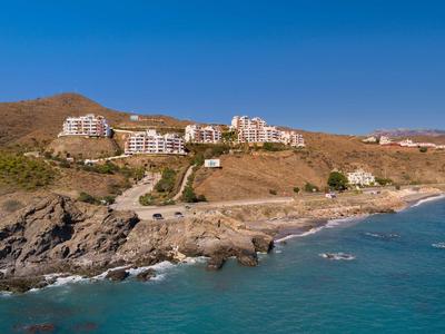 Küstenlandschaft mit Felsen, blauer See und mehreren weißen Gebäuden auf braunen Hügeln.