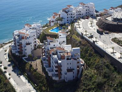 Weiße Wohngebäude am Hang mit Meerblick und Pool, umgeben von Straßen und Grünflächen.