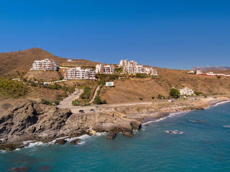 Küstenlandschaft mit Felsen, blauer See und mehreren weißen Gebäuden auf braunen Hügeln.