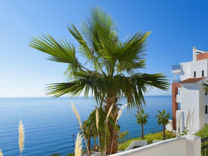 Meerblick mit blauen Himmel, Palmen und weiße Gebäude an der Küste bei Sonnenschein.
