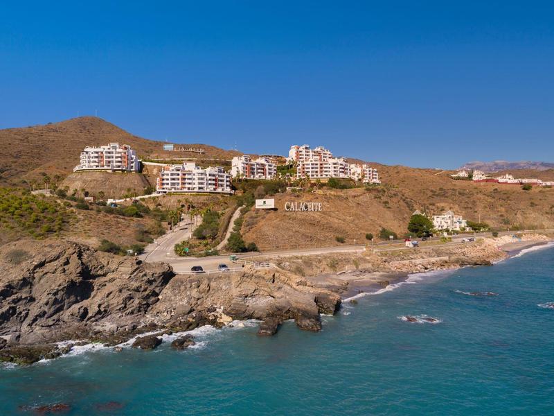 Hügel mit Wohngebäuden, Felsen und türkisfarbenem Meer unter klarem blauem Himmel.