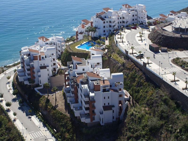 Weiße Wohngebäude am Hang mit Meerblick und Pool, umgeben von Straßen und Grünflächen.