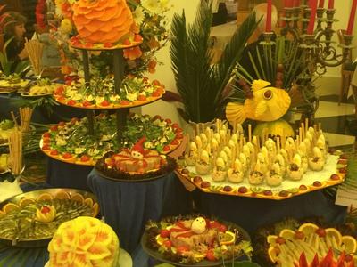 Buffet mit kunstvoll angerichteten Obst- und Gemüsetellern in warmem, gelbem Licht.