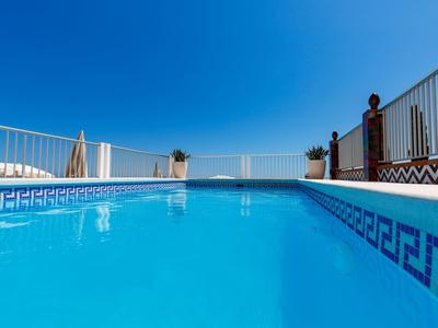 Blauer Pool mit sauberem Wasser, umgeben von weißem Geländer und klarem Himmel.