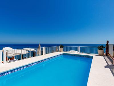 Ein klarer blauer Pool mit weißen Sonnenschirmen und Blick auf das offene Meer unter blauem Himmel.