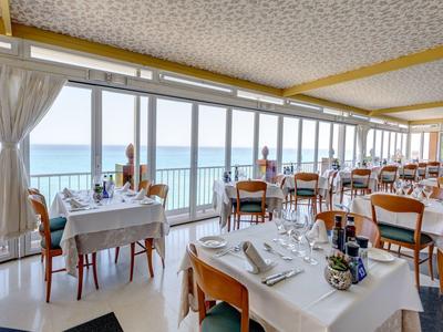 Helles Restaurant mit großen Fenstern, weißen Tischen und Blick aufs Meer.