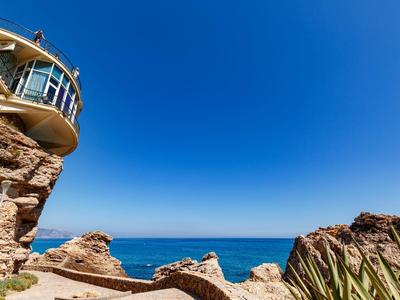 Schiffswartehaus auf Felsen über ruhigem blauen Meer unter klarem, tiefblauem Himmel.