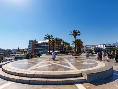 Große runde Plattform mit Sternmuster, umgeben von Palmen und Gebäuden unter klarem Himmel.