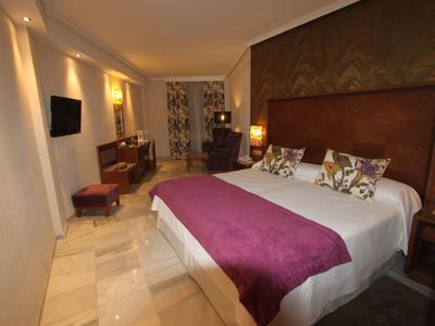 Modernes Schlafzimmer mit großem Bett, violettem Überwurf und warmem Licht.