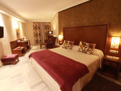 Hell beleuchtetes Schlafzimmer mit großem Bett, braunen Möbeln und rotem Bettüberwurf.