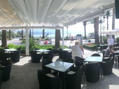 Großer, heller Innenbereich eines Cafés mit Tischen, Stühlen, großer Fensterfront und Snack-Bar-Schild.