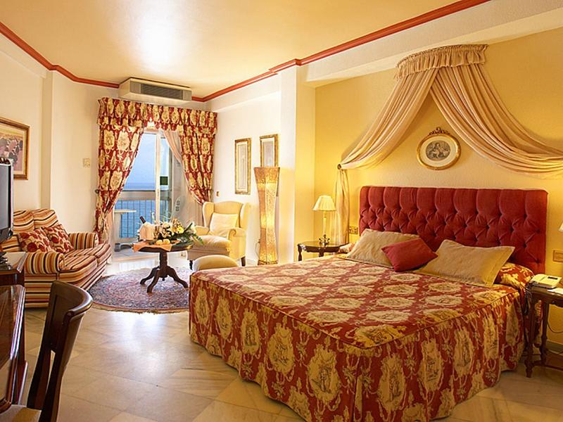 Promenade mit dunkler Bronzestatue eines Mannes, blauem Himmel und Bergen im Hintergrund.