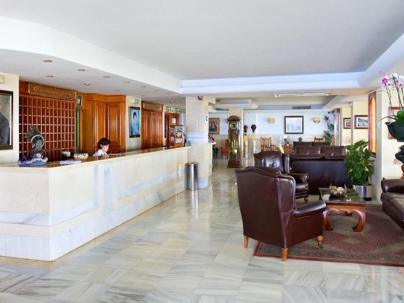 Helle Hotellobby mit marmornem Empfangstresen, Ledersesseln und Pflanzenarrangements.