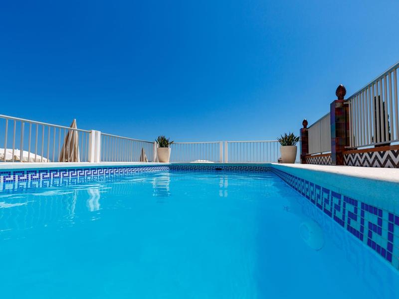 Blauer Pool mit sauberem Wasser, umgeben von weißem Geländer und klarem Himmel.