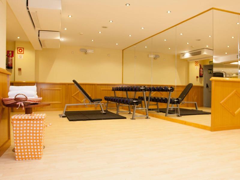 Leerer Fitnessraum mit Hantelbänken, Holzvertäfelung, großer Spiegelwand und gelben Wänden.