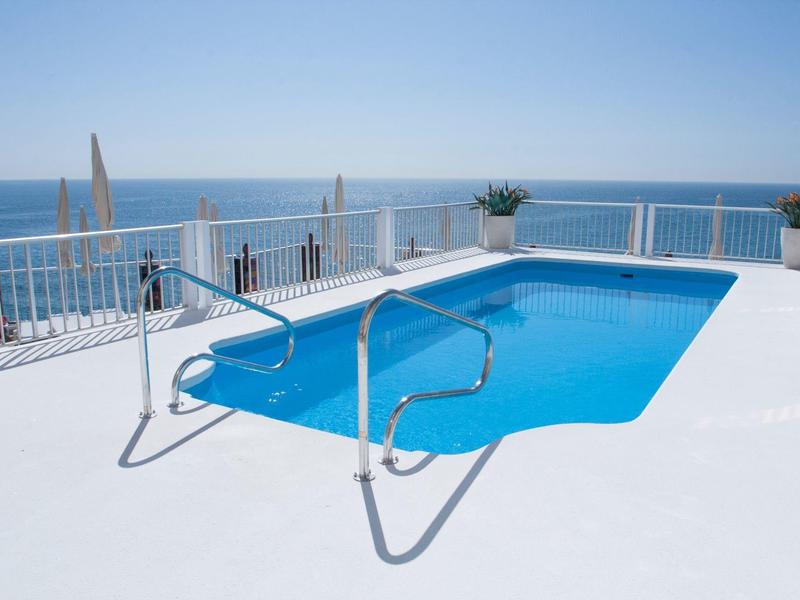 Blauer Pool auf weißer Terrasse mit Meerblick und bewölktem Himmel im Hintergrund.