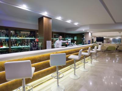 Moderner Hotelbarbereich mit beleuchtetem Tresen und weißen Barhockern.