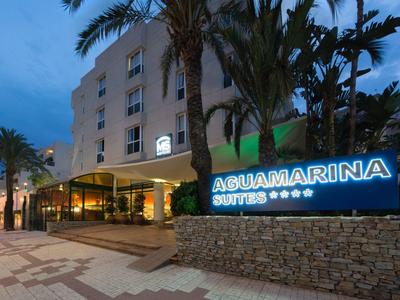 Hotelgebäude mit Palmendekoration und beleuchtetem AGUAMARINA Suites Schild bei Dämmerung.
