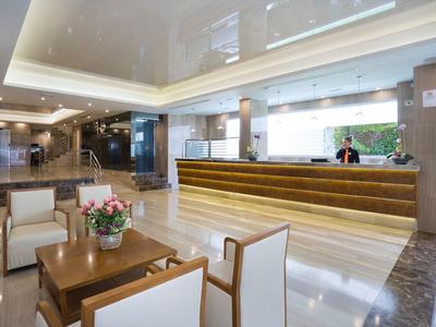 Helle, moderne Hotellobby mit Holzmöbeln, Rezeption und Blumenarrangement auf Tisch.