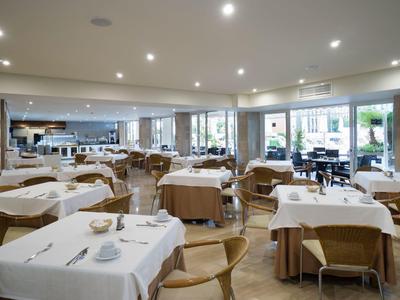 Helles Restaurant mit gedeckten Tischen und Holzmöbeln, große Fenster bieten Blick nach draußen.