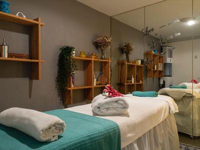 Hell beleuchteter Wellnessraum mit zwei Massageliegen, Handtüchern und Holzwandregalen mit Dekoration.