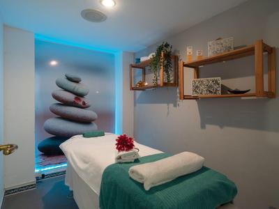 Behandlungsraum mit Massagebett, grüner Decke, Handtüchern und beruhigender Wandkunst.