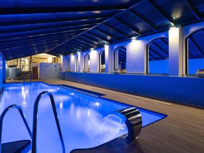 Innenpool mit blauer Beleuchtung und großen Fenstern in einem Hotel.