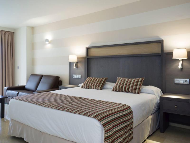 Modernes Hotelzimmer mit großem Doppelbett, Nachttischen und Sofa am Fenster.