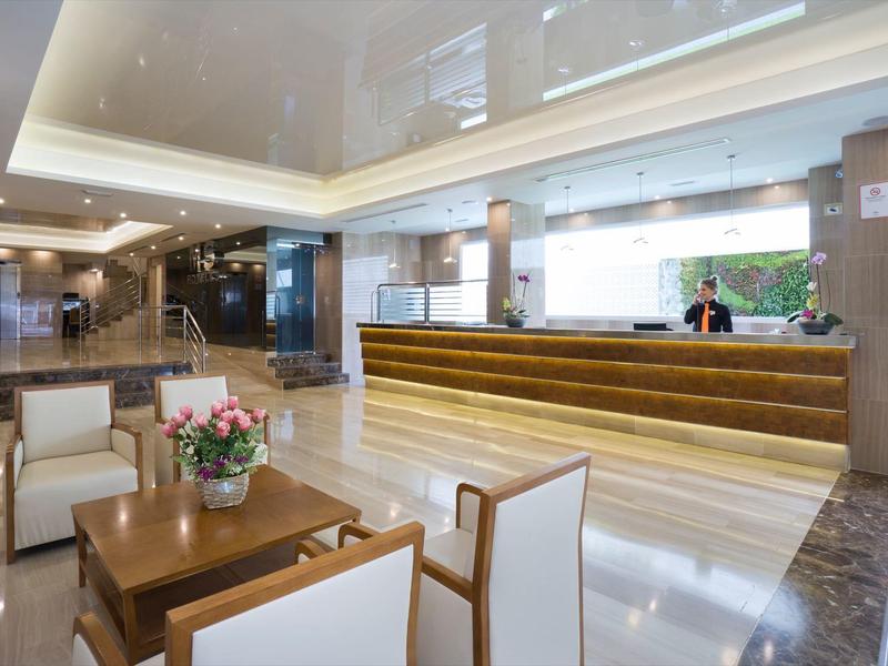 Helle, moderne Hotellobby mit Holzmöbeln, Rezeption und Blumenarrangement auf Tisch.