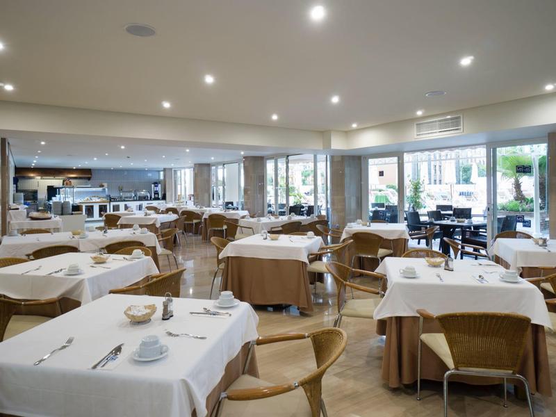 Helles Restaurant mit gedeckten Tischen und Holzmöbeln, große Fenster bieten Blick nach draußen.