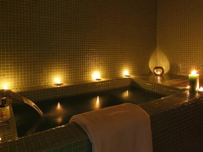 Ein dunkles Bad mit warmem Licht, Kerzen und einem Handtuch am Rand der Wanne.