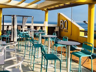 Offenes Strandcafé mit türkisfarbenen Stühlen, Tischen und Blick auf das Meer bei Sonnenschein.