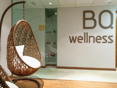 Moderner Wellness-Bereich mit hängendem Korbsessel und bequemen weißen Kissen an heller Wand.