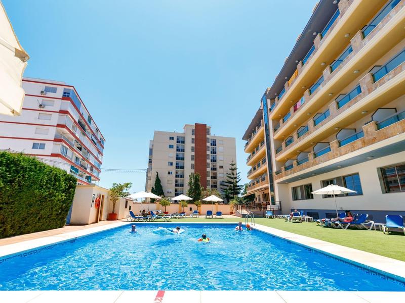 Schwimmbad mit klar blauem Wasser, umgeben von mehrstöckigen Wohngebäuden und Sonnenliegen.