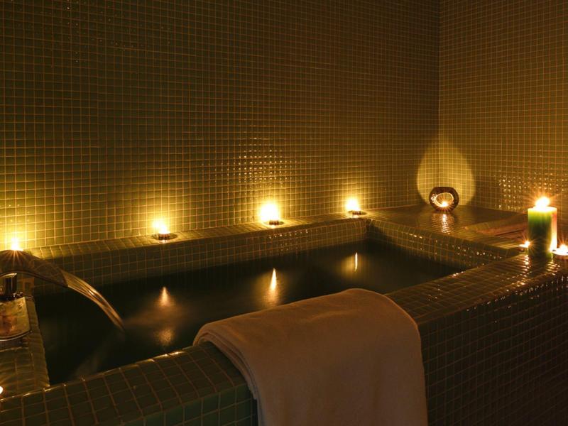 Ein dunkles Bad mit warmem Licht, Kerzen und einem Handtuch am Rand der Wanne.